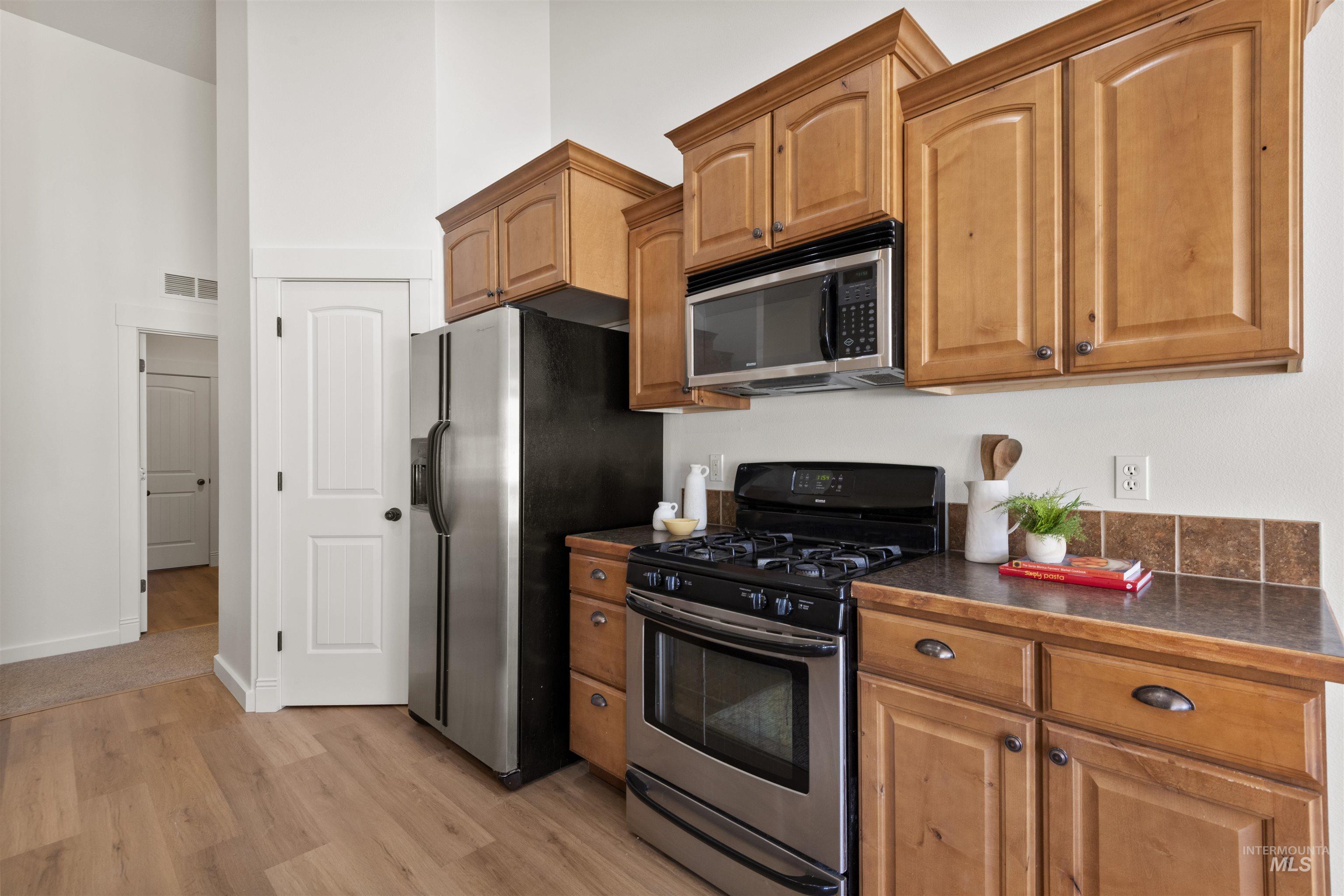 Kitchen with stainless steel appliances, dark countertops, light wood-type flooring, a high ceiling, and brown cabinetry