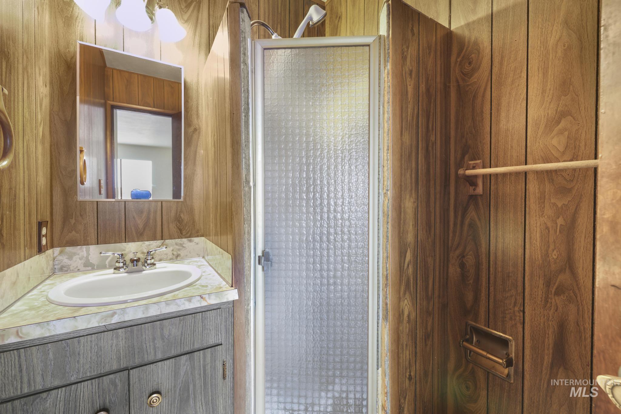 Bathroom featuring wood walls, a stall shower, and vanity