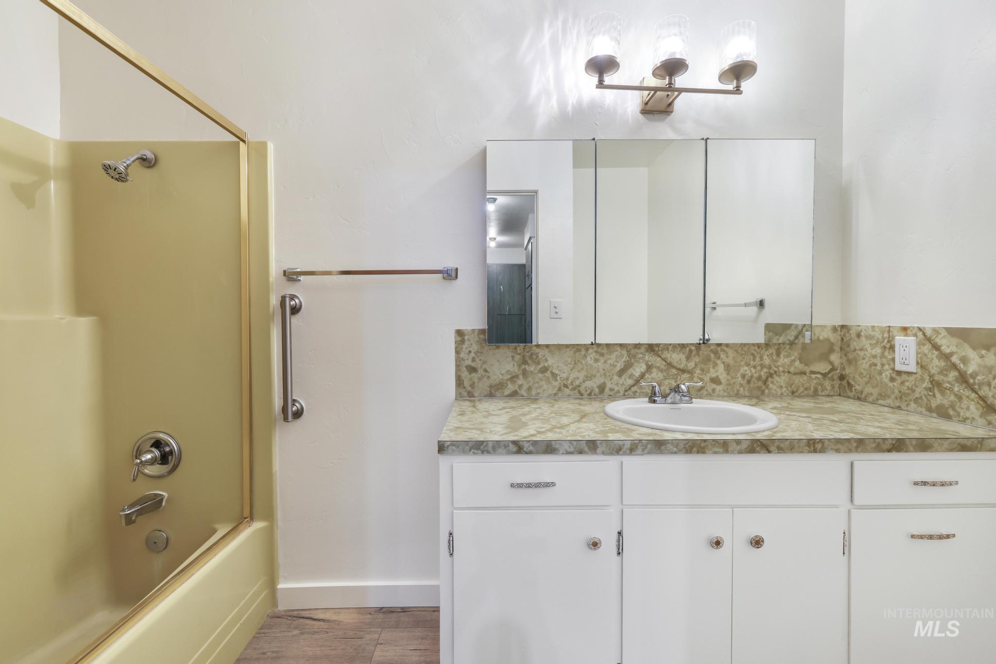 Full bath with bathing tub / shower combination, vanity, and light wood-style floors