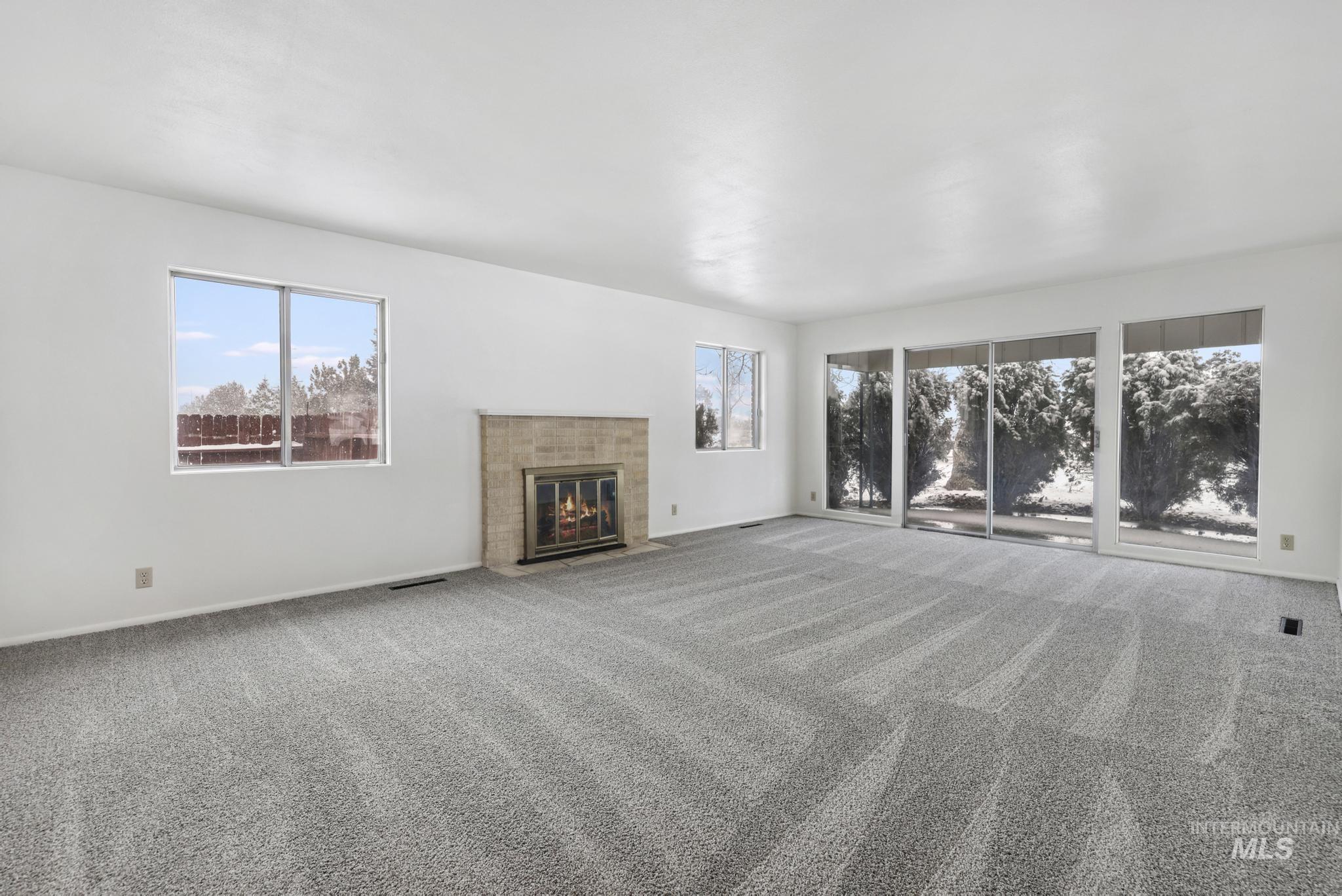 Unfurnished living room with plenty of natural light, carpet flooring, and a tiled fireplace