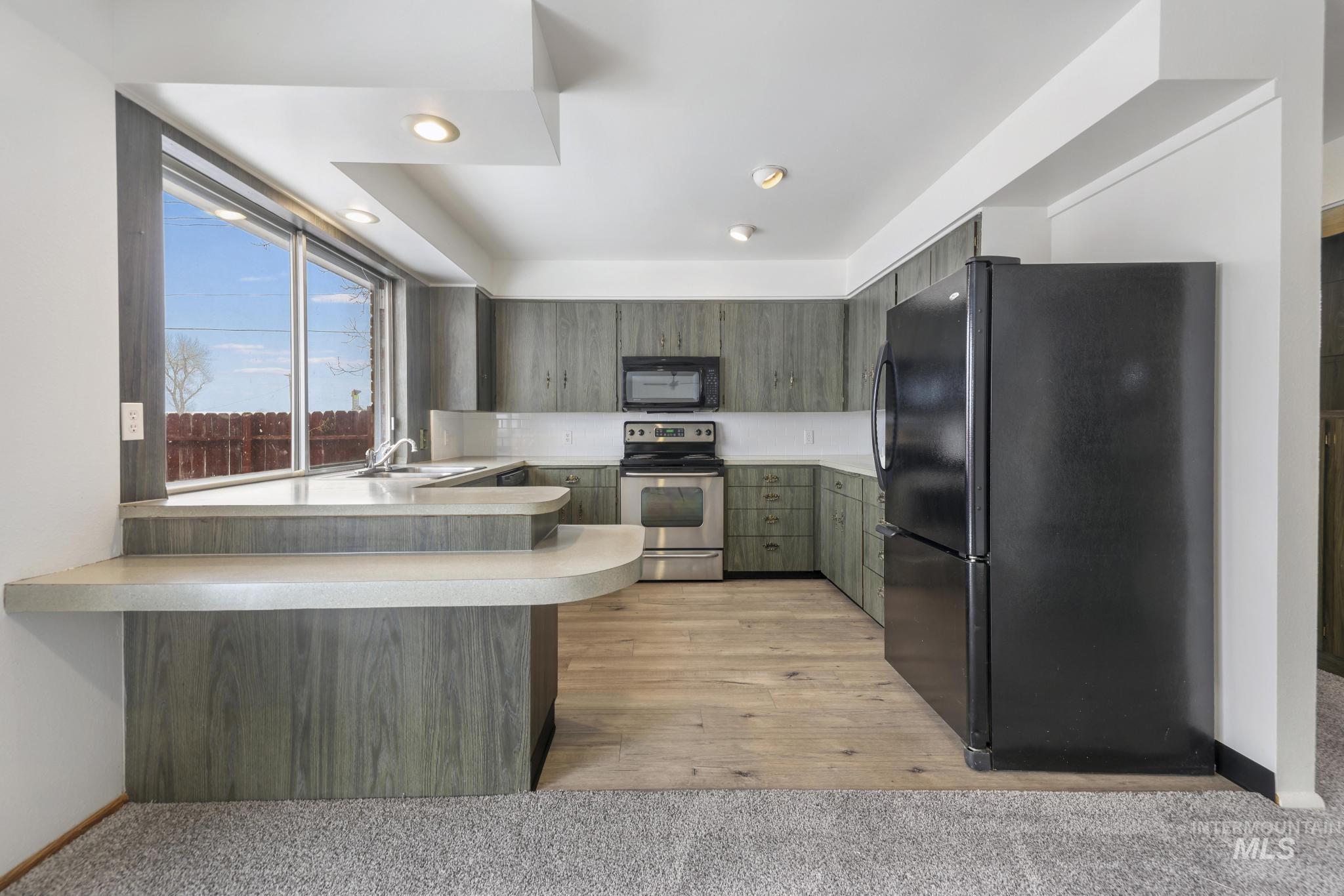 Kitchen with black appliances, light countertops, a peninsula, recessed lighting, and light colored carpet