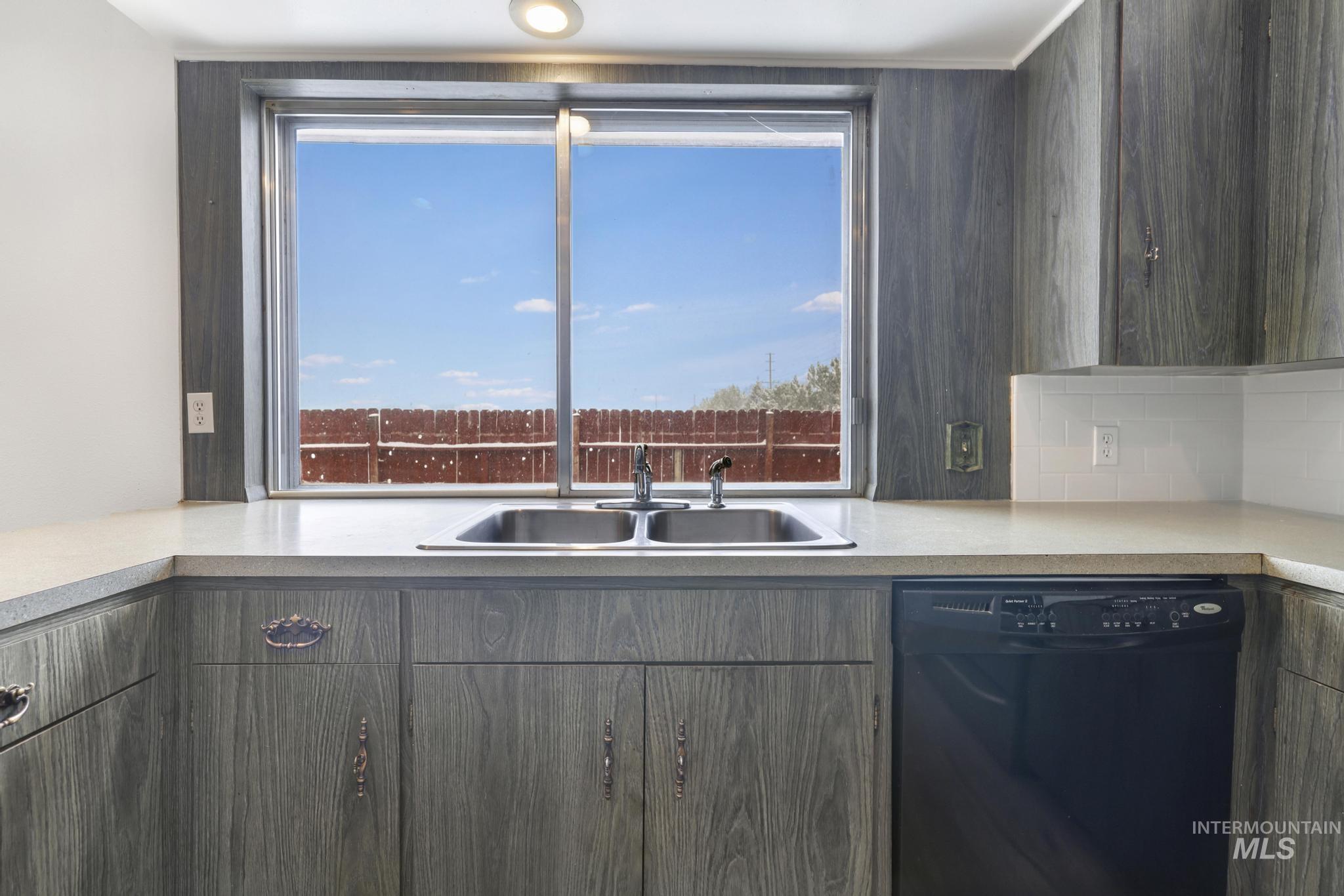 Kitchen with black dishwasher, light countertops, plenty of natural light, and decorative backsplash
