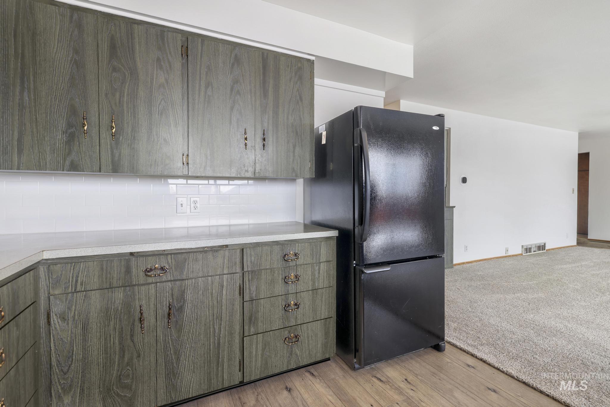 Kitchen featuring freestanding refrigerator, light countertops, decorative backsplash, and light wood-style floors