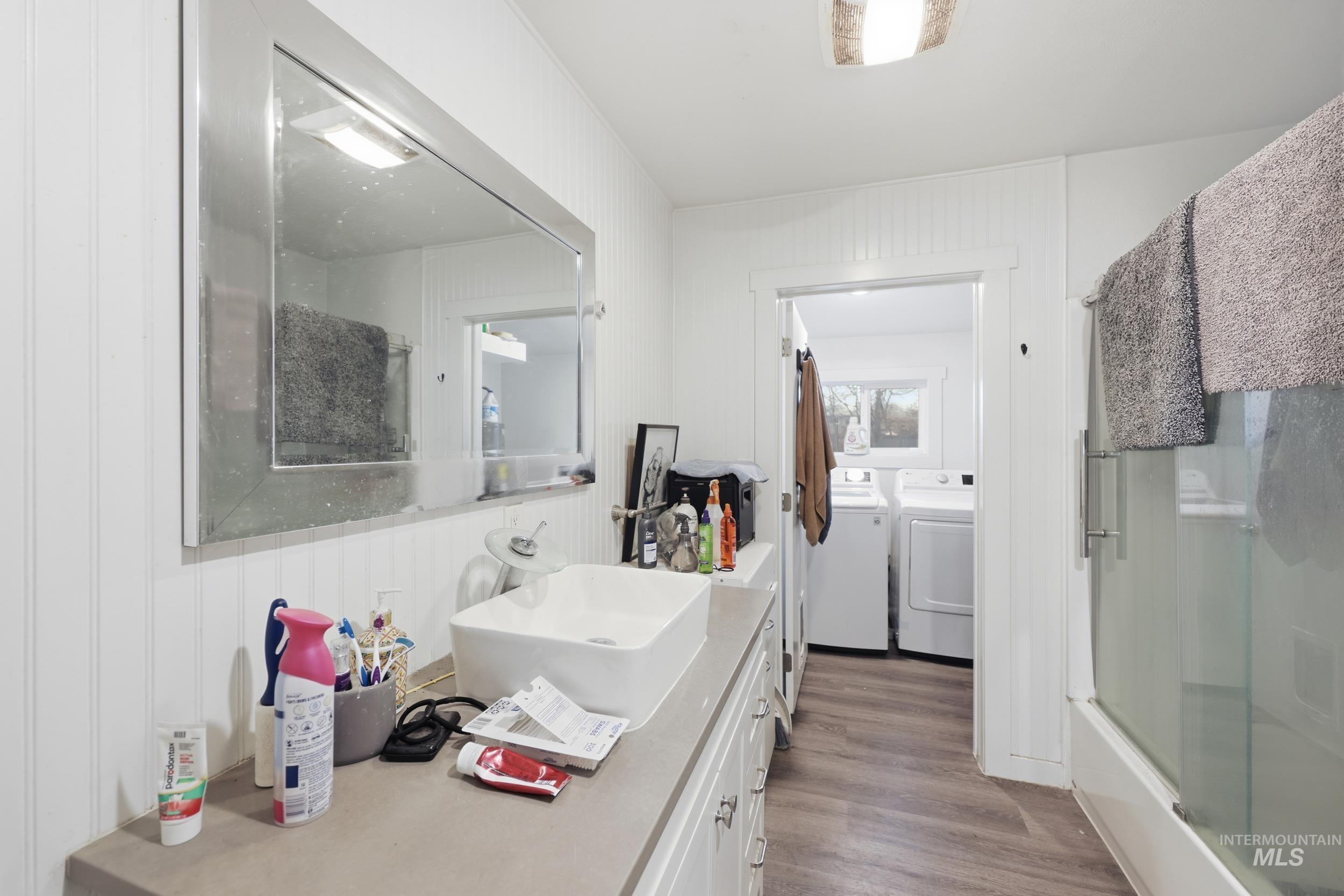 Bathroom with vanity, dark wood finished floors, bath / shower combo with glass door, and washing machine and dryer