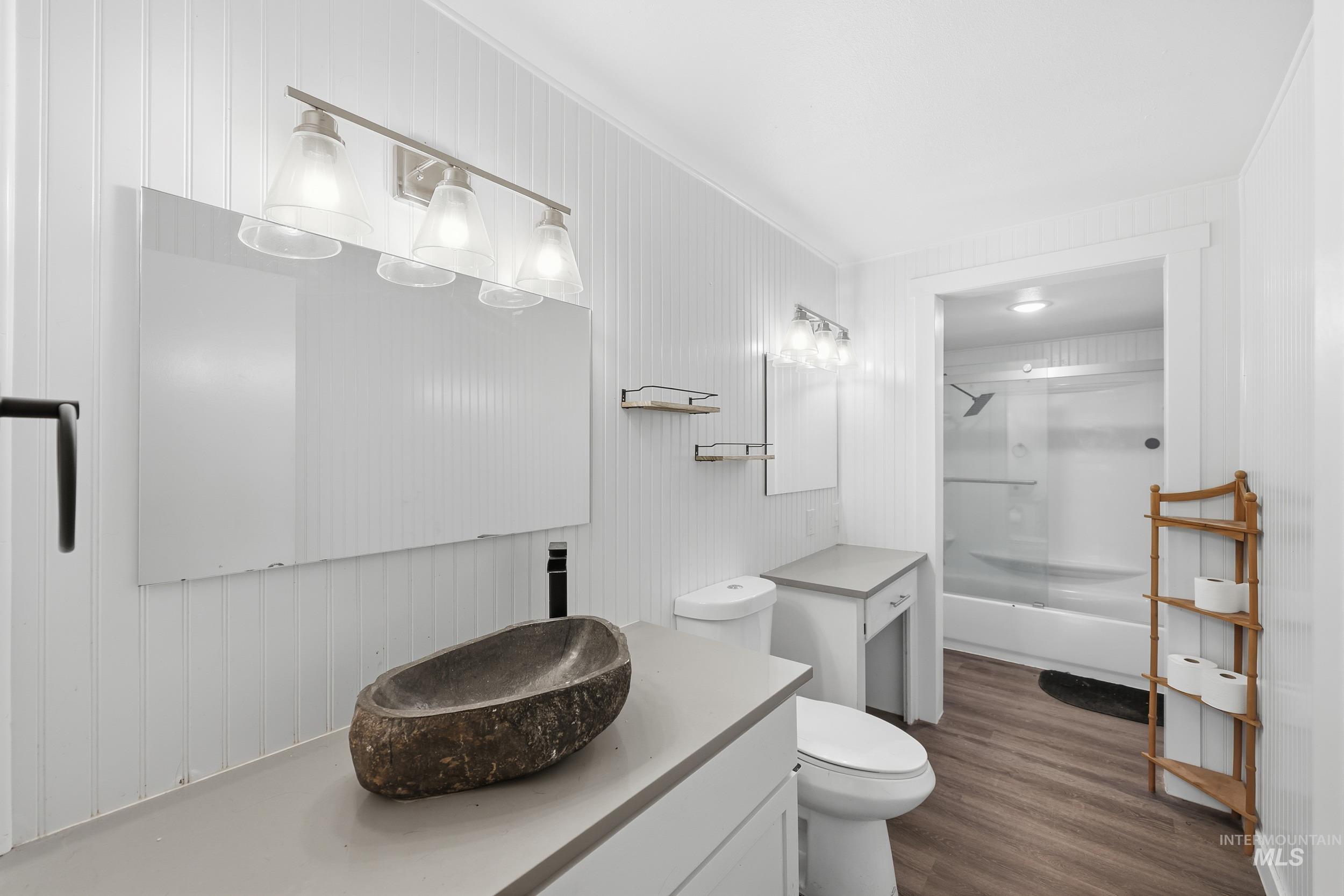 Full bath with vanity,  shower combination, dark wood-style floors, and wooden walls