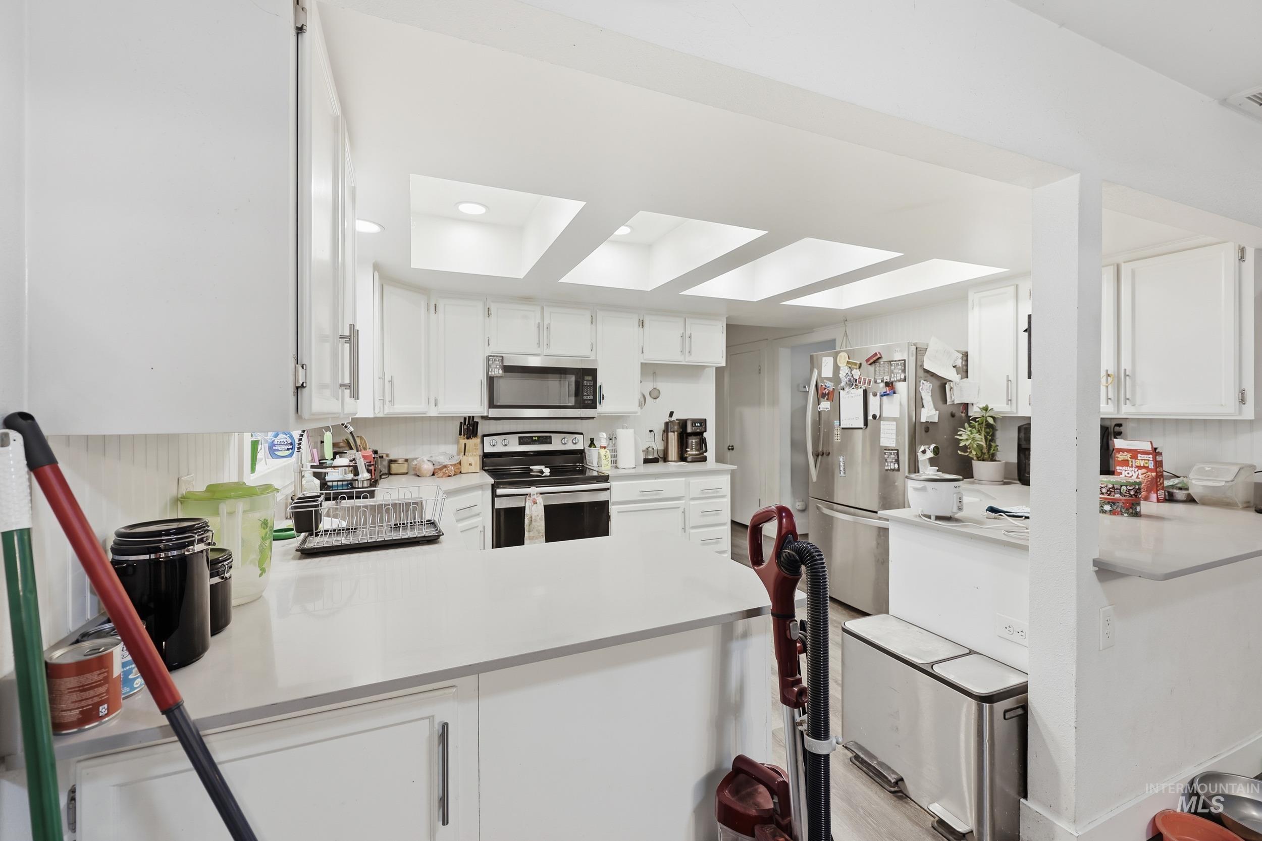 Kitchen with a peninsula, white cabinetry, stainless steel appliances, recessed lighting, and light wood finished floors