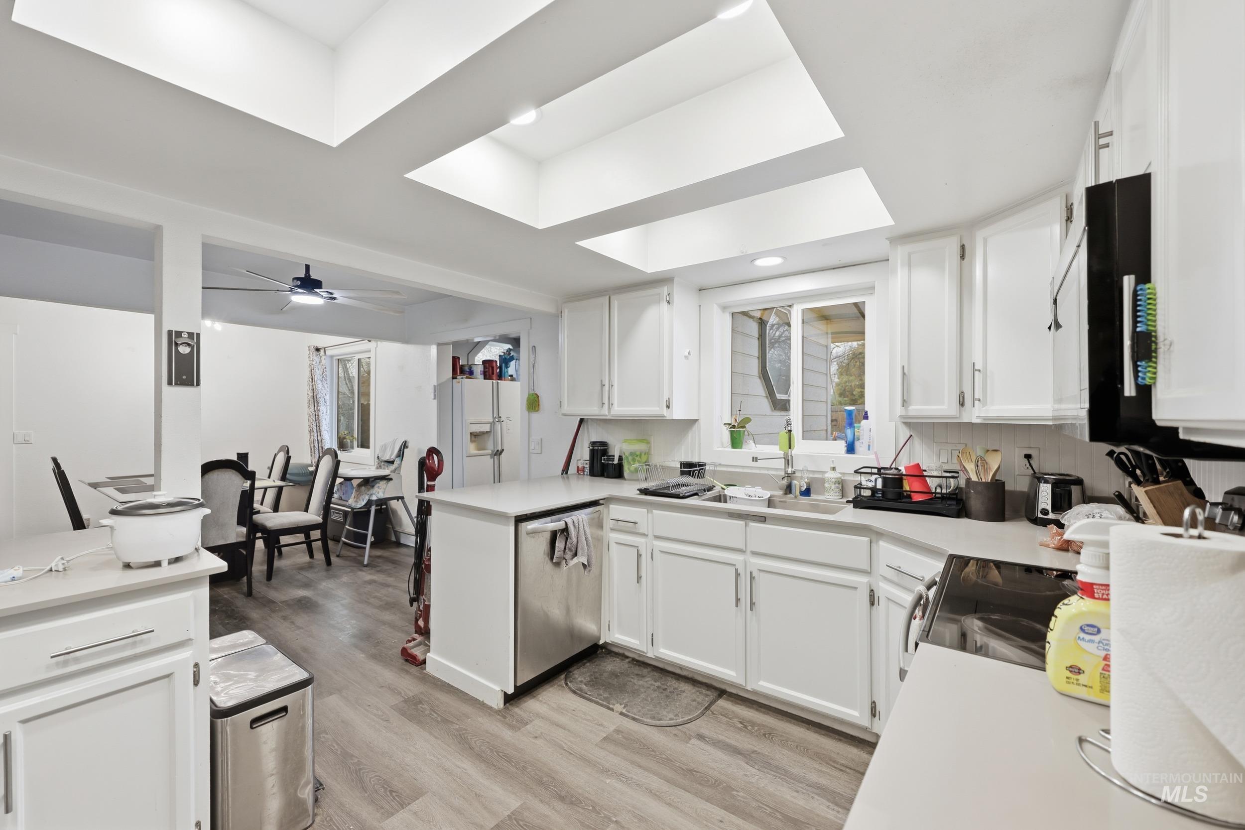 Kitchen with white cabinetry, light countertops, dishwasher, white fridge with ice dispenser, and light wood-type flooring