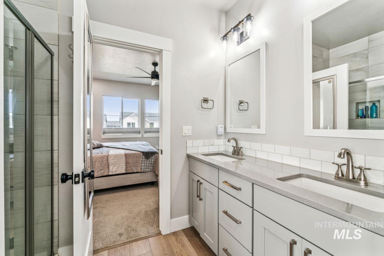Ensuite bathroom featuring a shower stall, double vanity, a ceiling fan, and light wood-style flooring