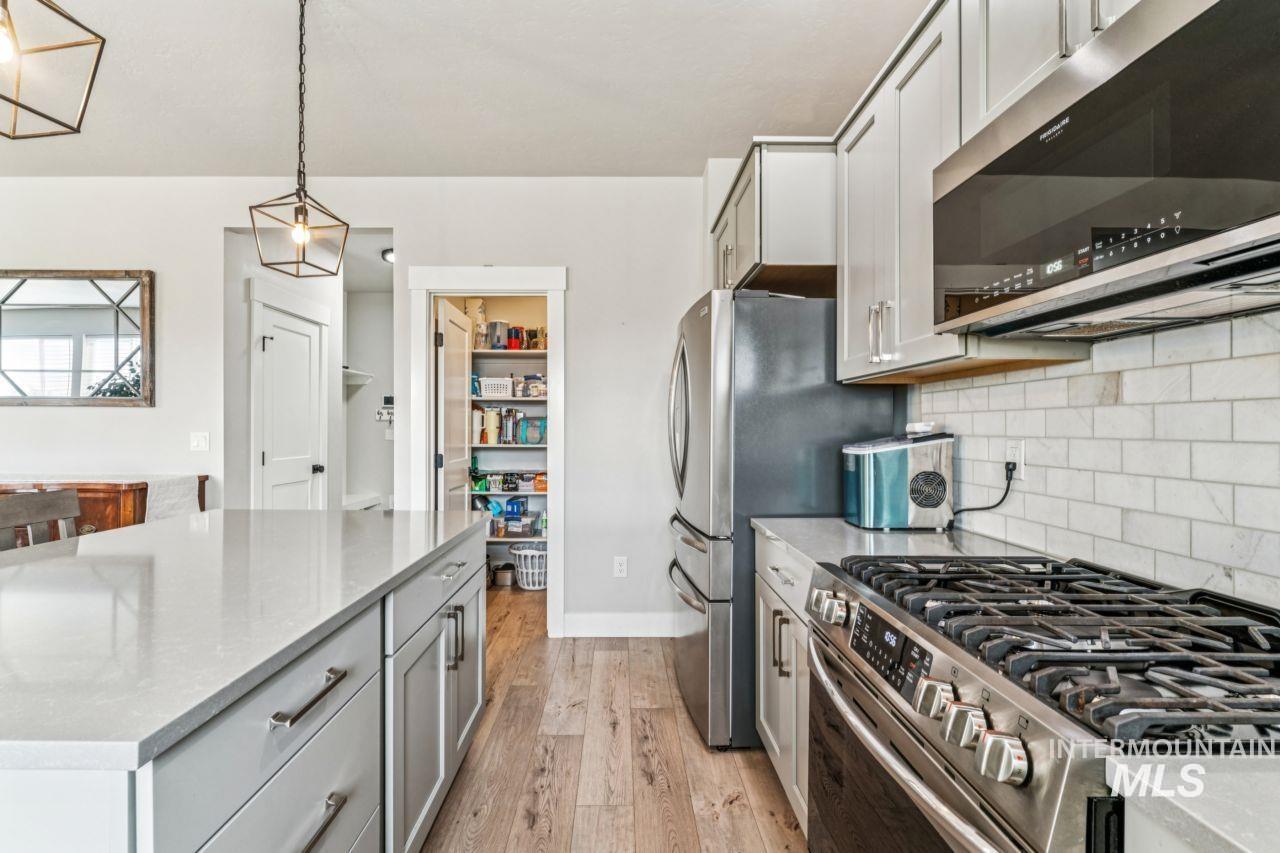 Kitchen featuring stainless steel appliances, hanging light fixtures, light stone countertops, gray cabinetry, and light wood-style floors