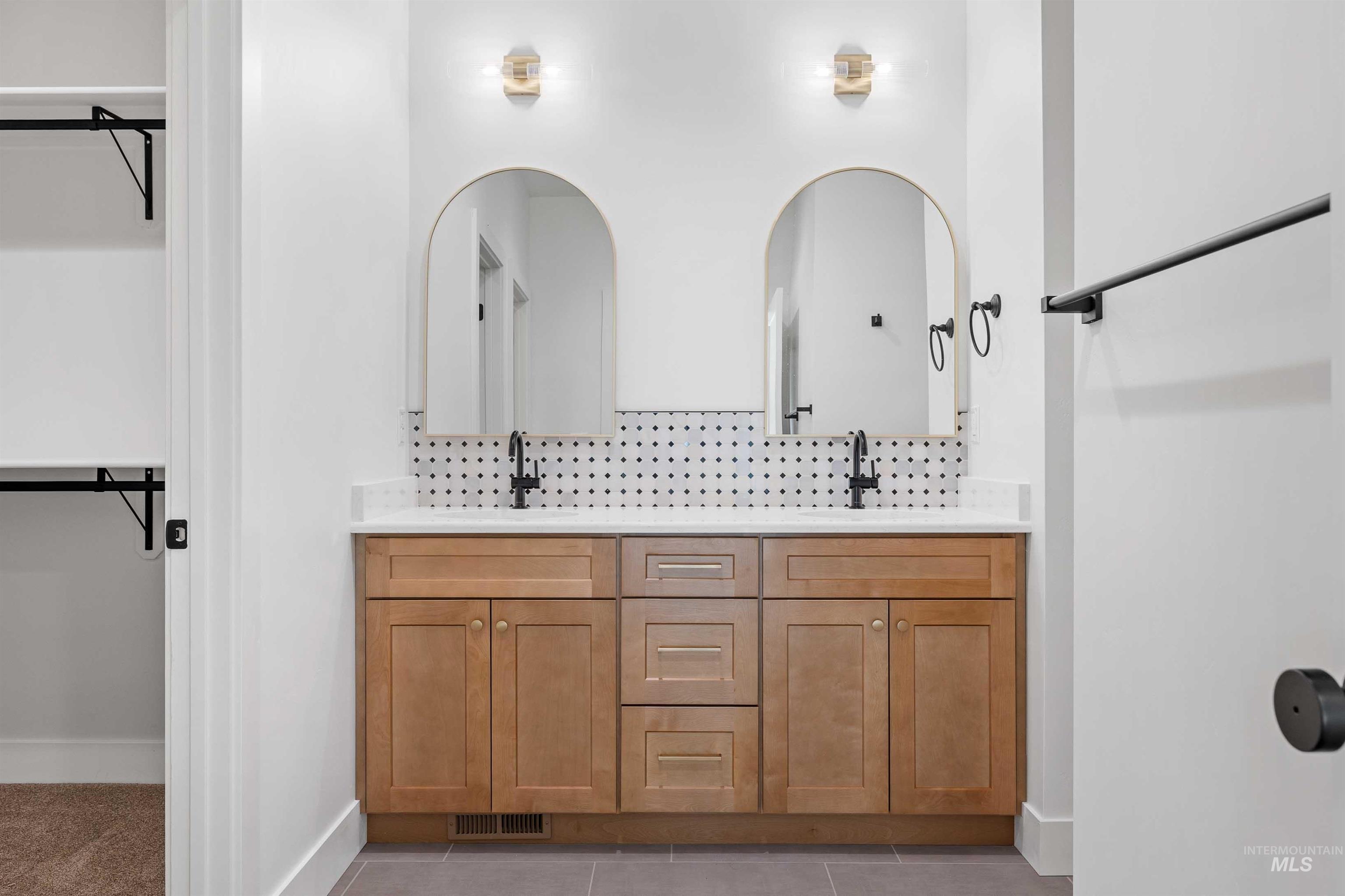 Bathroom with a spacious closet, tasteful backsplash, double vanity, and light tile patterned floors