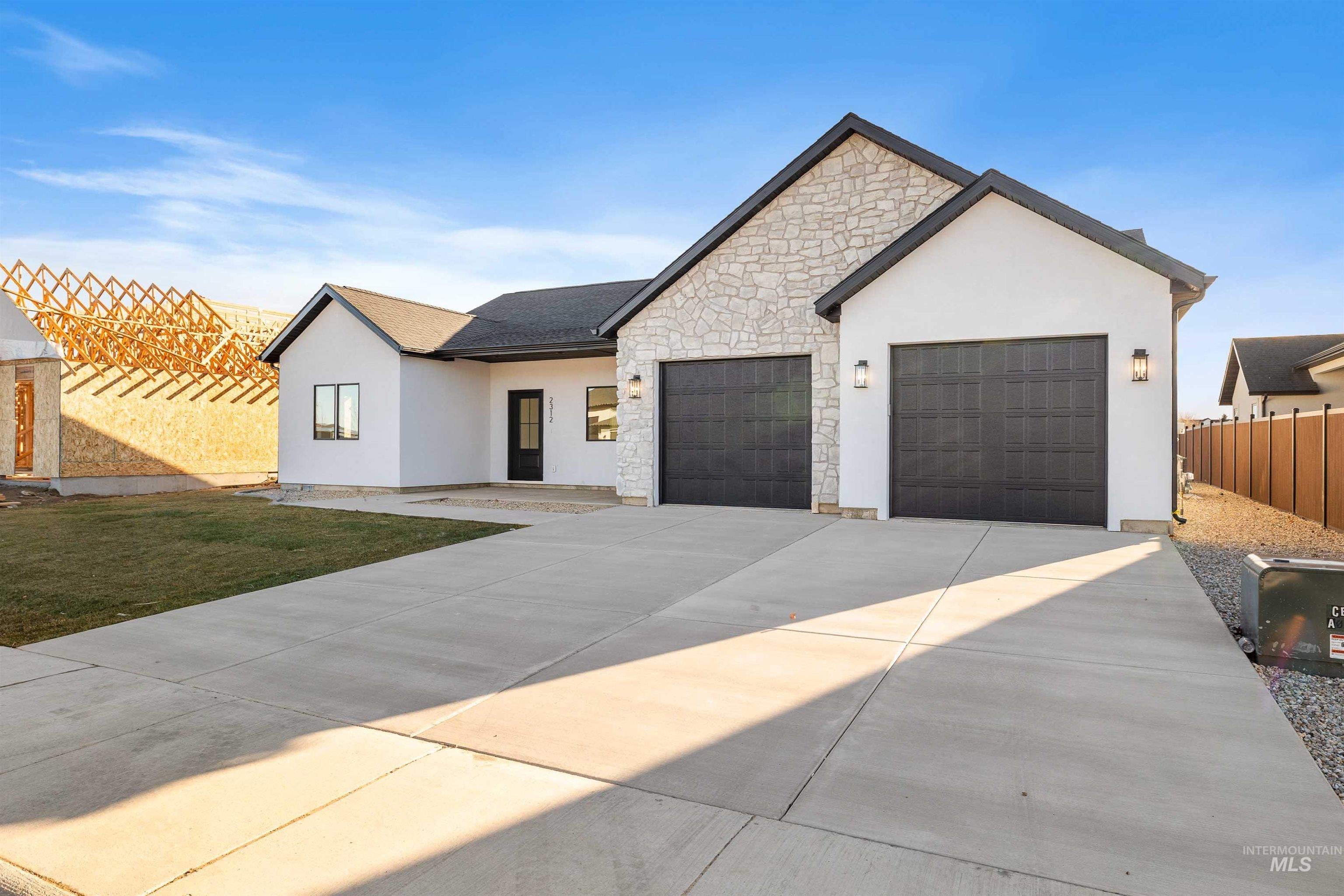 View of front of property with concrete driveway, stucco siding, stone siding, and an attached garage