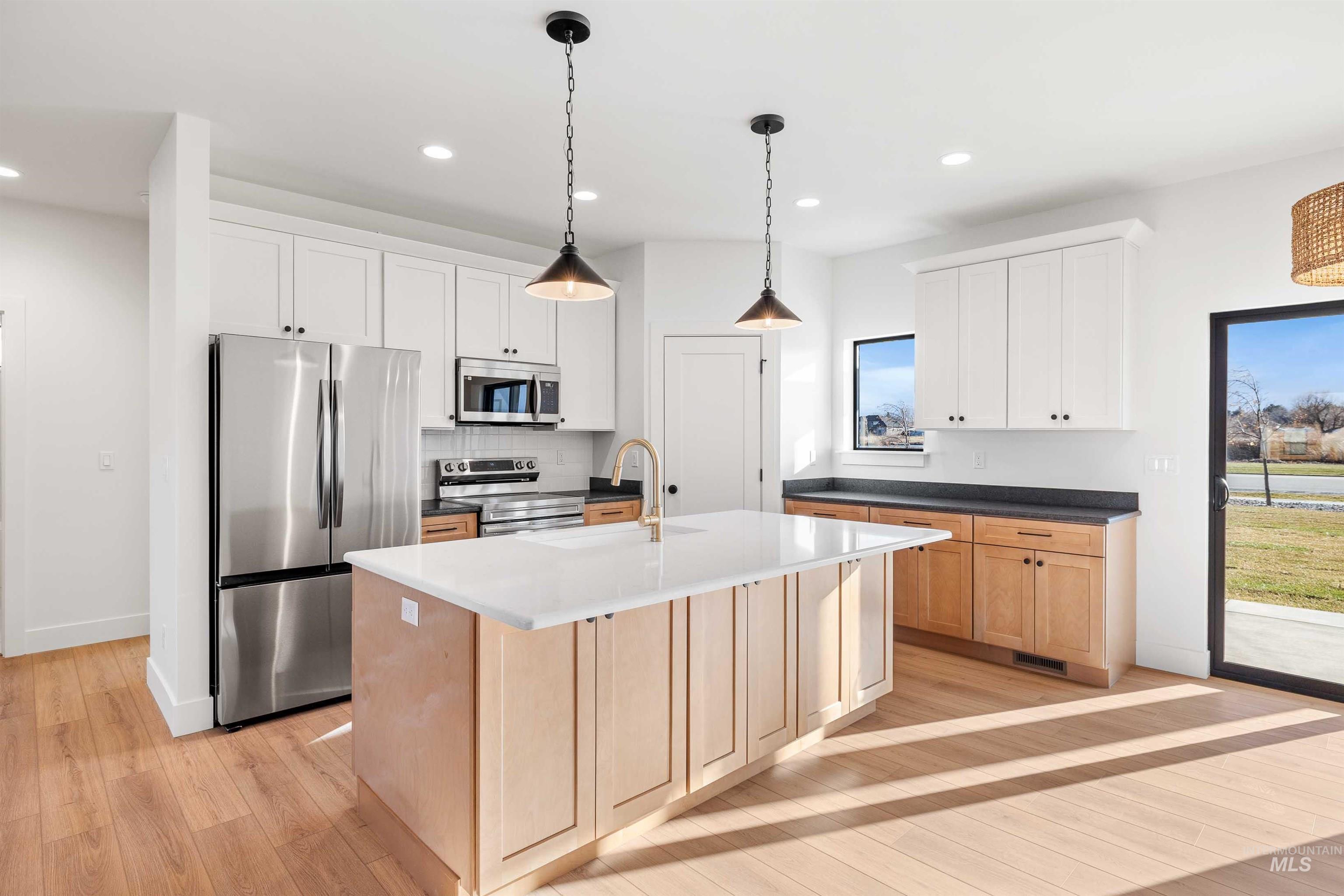 Kitchen with appliances with stainless steel finishes, a kitchen island with sink, recessed lighting, light wood-style floors, and hanging light fixtures
