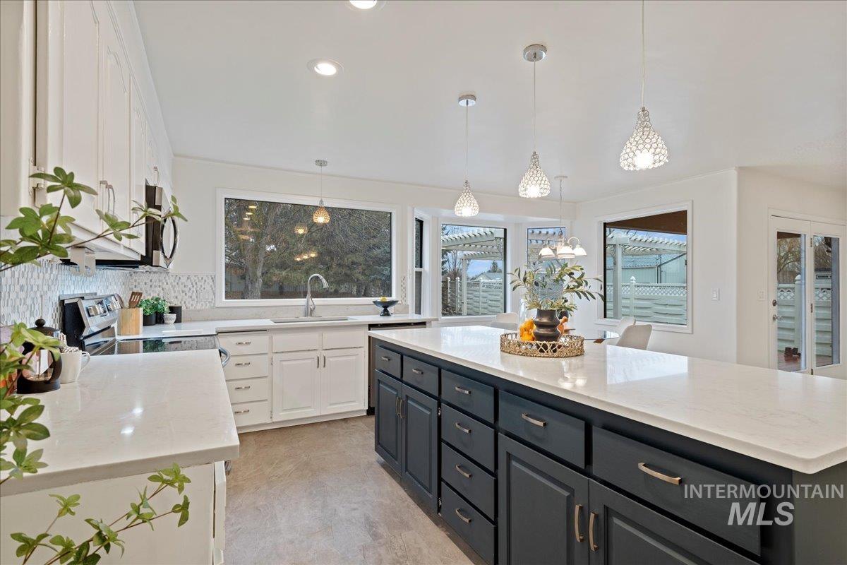 Kitchen featuring white cabinetry, light stone counters, hanging light fixtures, appliances with stainless steel finishes, and tasteful backsplash