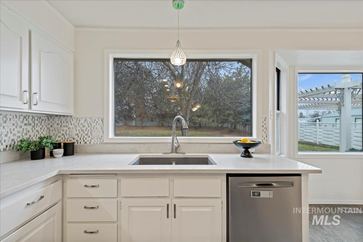 Kitchen featuring stainless steel dishwasher, white cabinetry, light stone countertops, hanging light fixtures, and wood finished floors