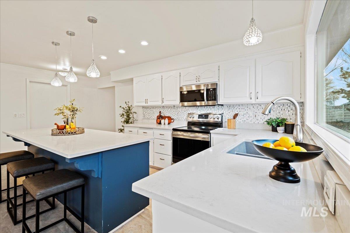 Kitchen with white cabinets, decorative light fixtures, a breakfast bar area, stainless steel appliances, and light stone countertops