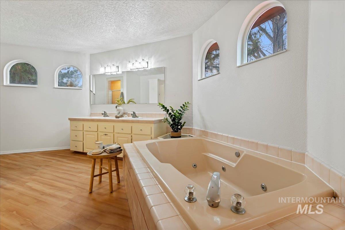 Full bathroom with a whirlpool tub, double vanity, a textured ceiling, light wood-style floors, and healthy amount of natural light