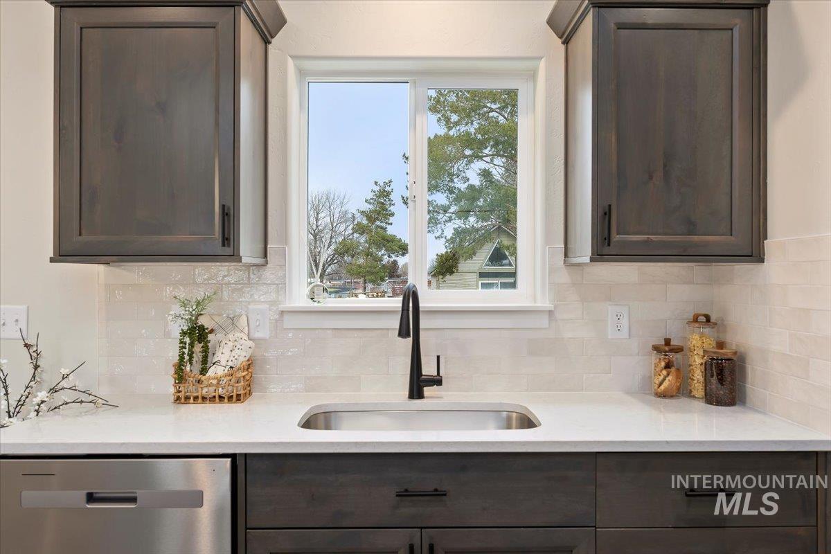 Kitchen featuring dark brown cabinets, stainless steel dishwasher, light stone countertops, and backsplash