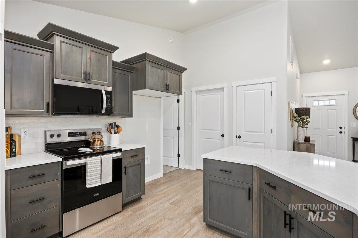 Kitchen with stainless steel appliances, dark brown cabinets, light stone countertops, decorative backsplash, and recessed lighting