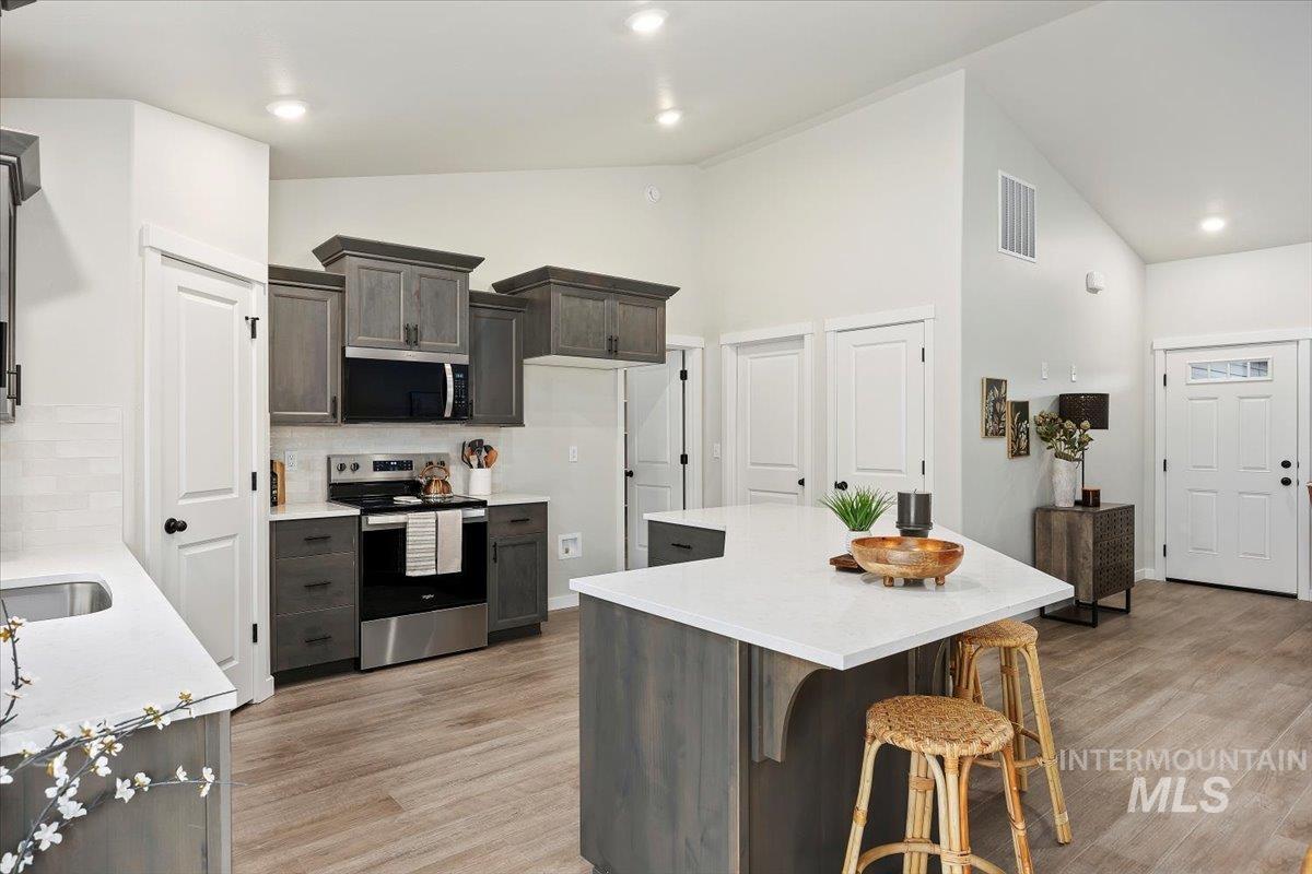Kitchen featuring stainless steel appliances, a center island, backsplash, light wood-style flooring, and high vaulted ceiling