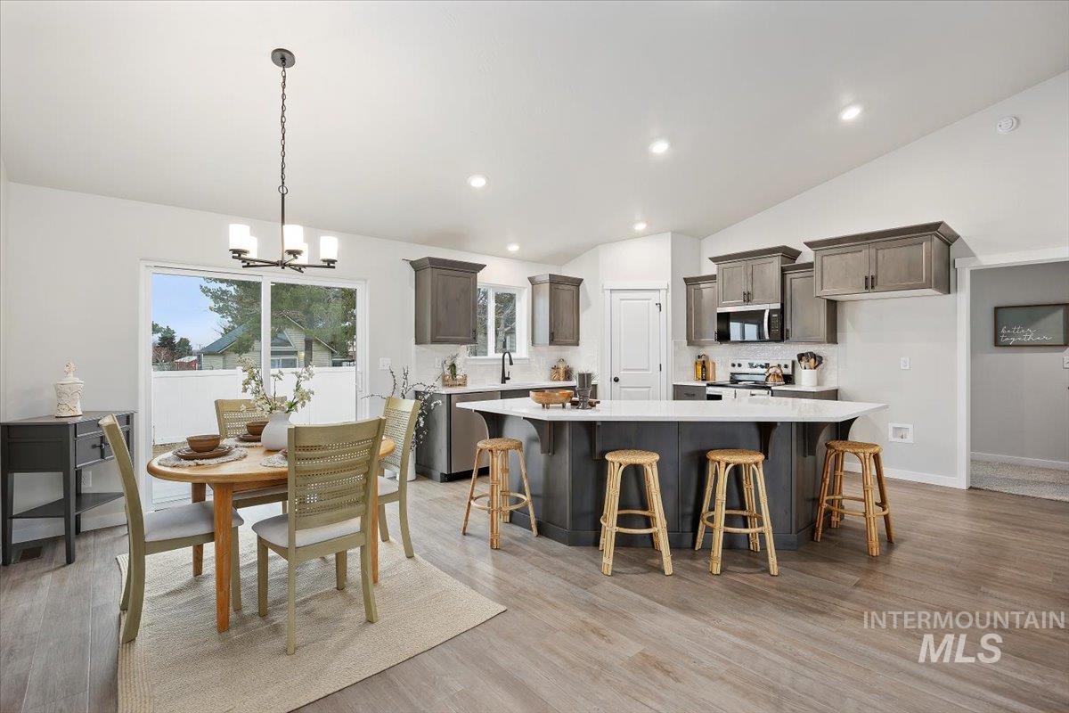 Kitchen with a breakfast bar, decorative light fixtures, a kitchen island, light wood-style floors, and lofted ceiling