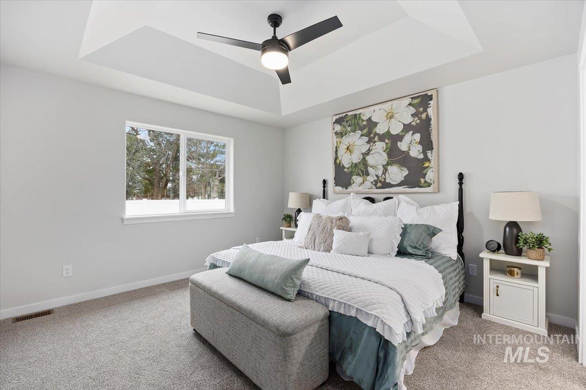 Bedroom with a raised ceiling, a ceiling fan, and light colored carpet