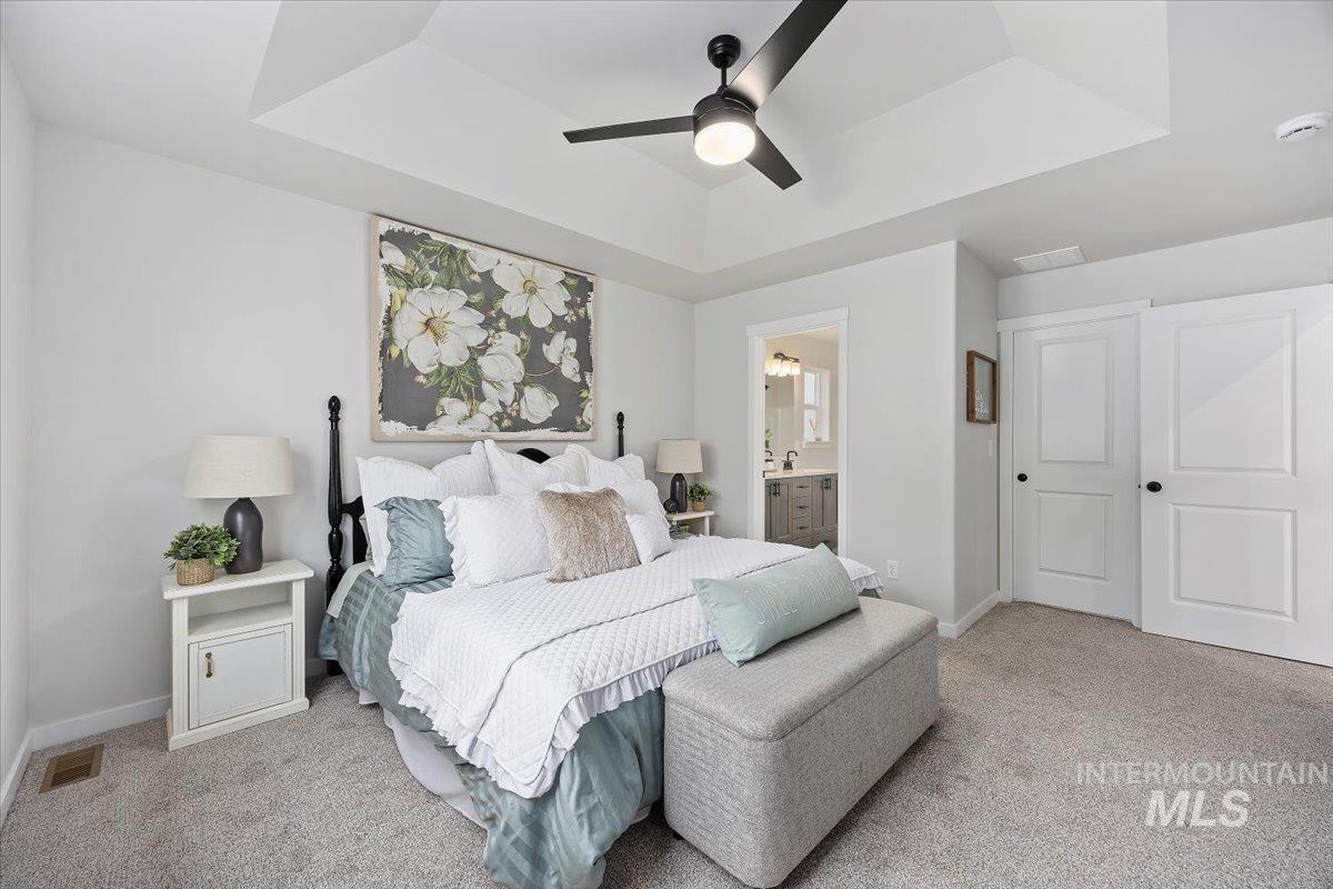 Bedroom featuring a raised ceiling, light carpet, ceiling fan, and ensuite bathroom
