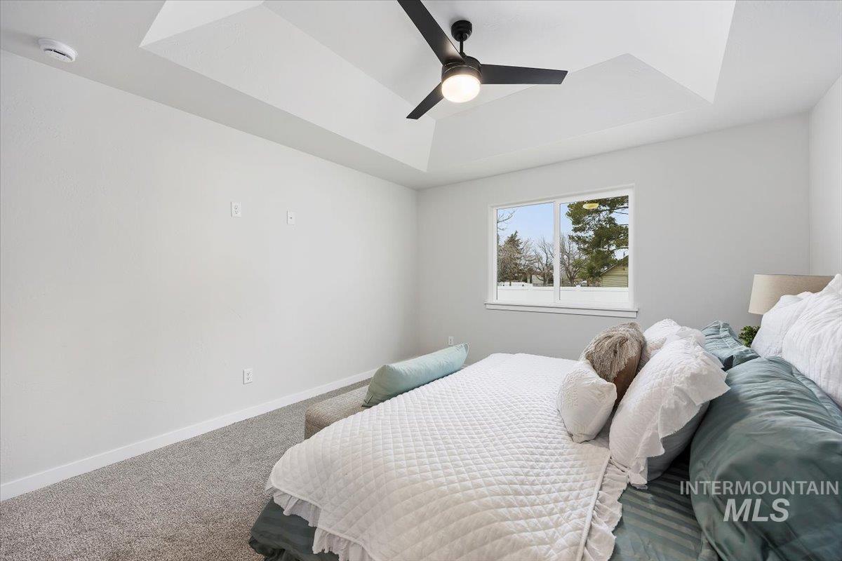 Bedroom with a tray ceiling, carpet floors, and a ceiling fan