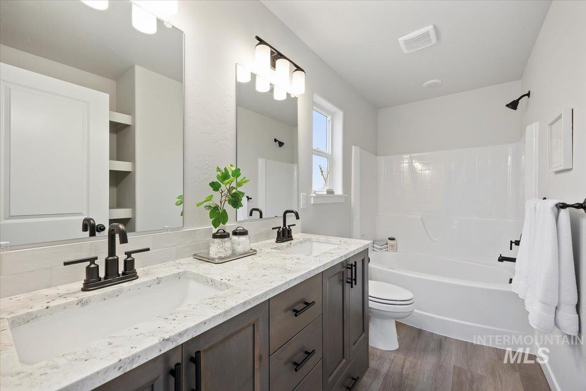 Bathroom featuring double vanity, shower / tub combination, and dark wood finished floors