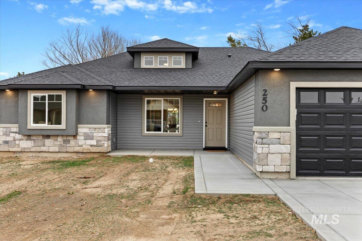 View of front of home with stone siding, a garage, covered porch, and roof with shingles