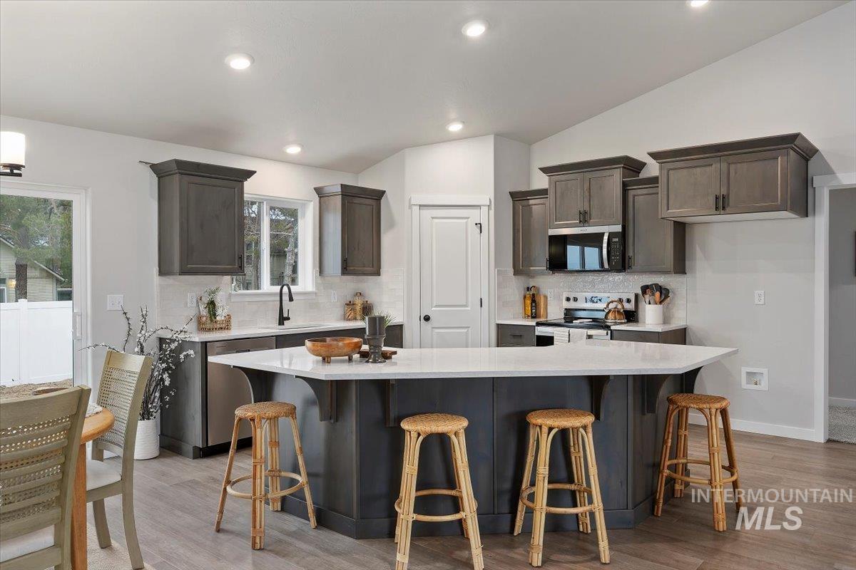 Kitchen featuring lofted ceiling, appliances with stainless steel finishes, tasteful backsplash, a kitchen bar, and light stone countertops