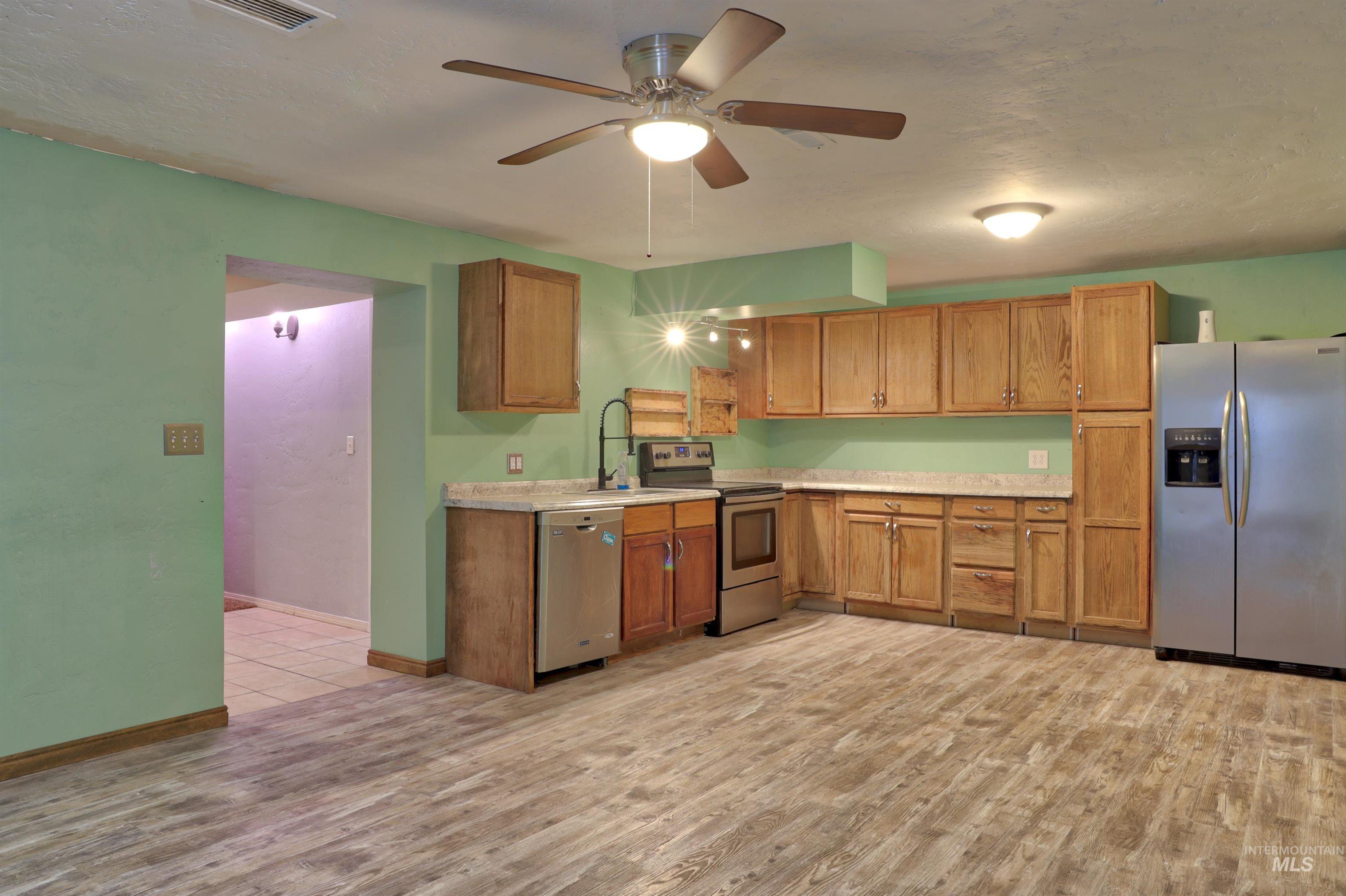 Kitchen featuring appliances with stainless steel finishes, light countertops, brown cabinets, a ceiling fan, and a textured ceiling