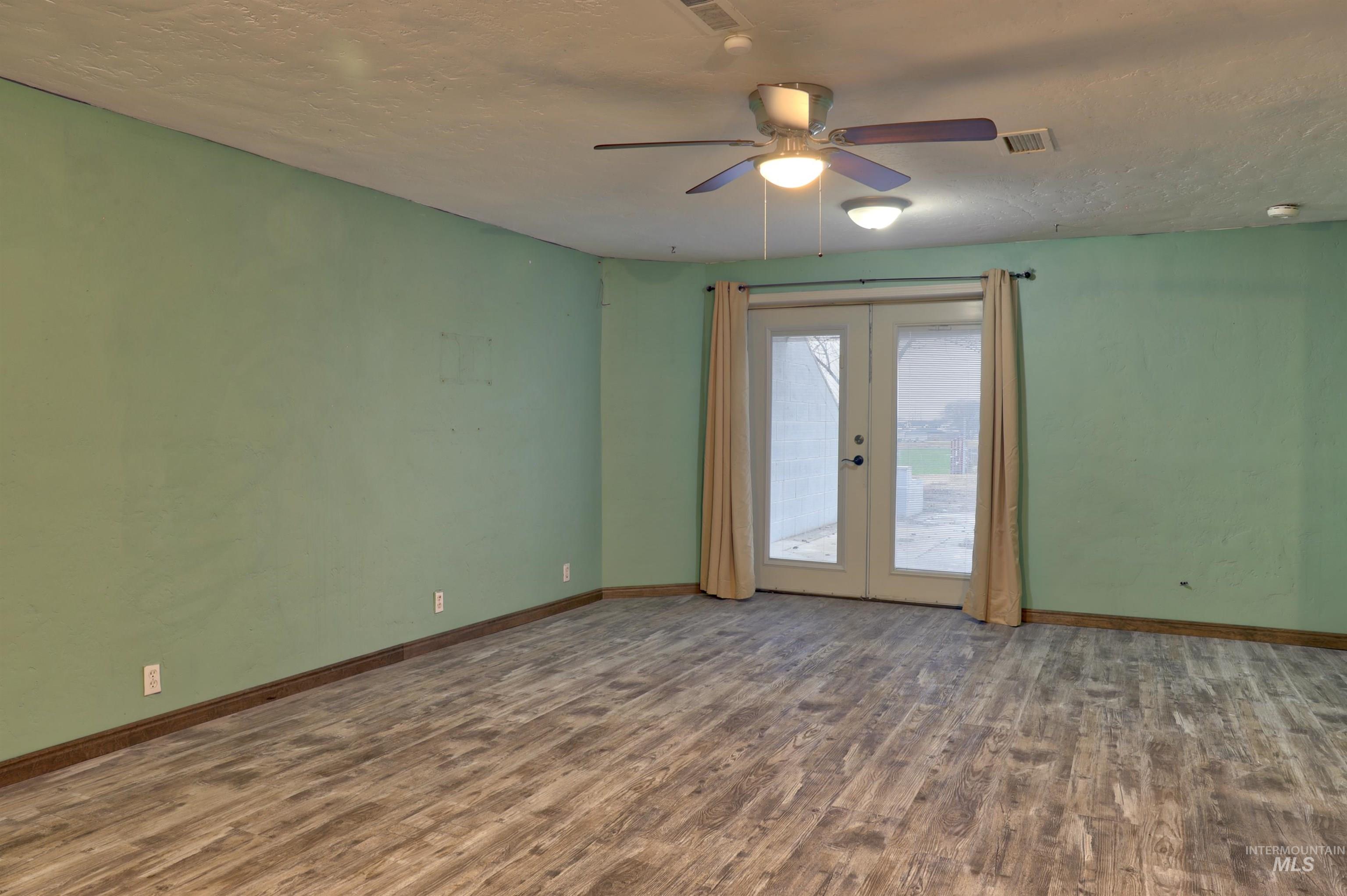 Downstairs living room with dark wood finished floors, ceiling fan & French doors to the backyard.