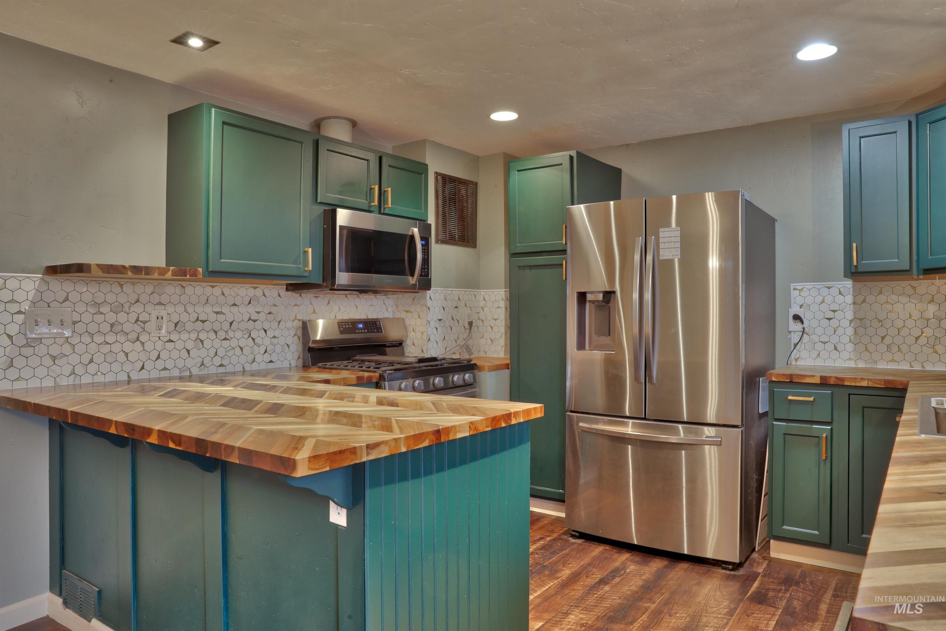 Kitchen featuring green cabinets, butcher block countertops, appliances with stainless steel finishes, a peninsula, and backsplash