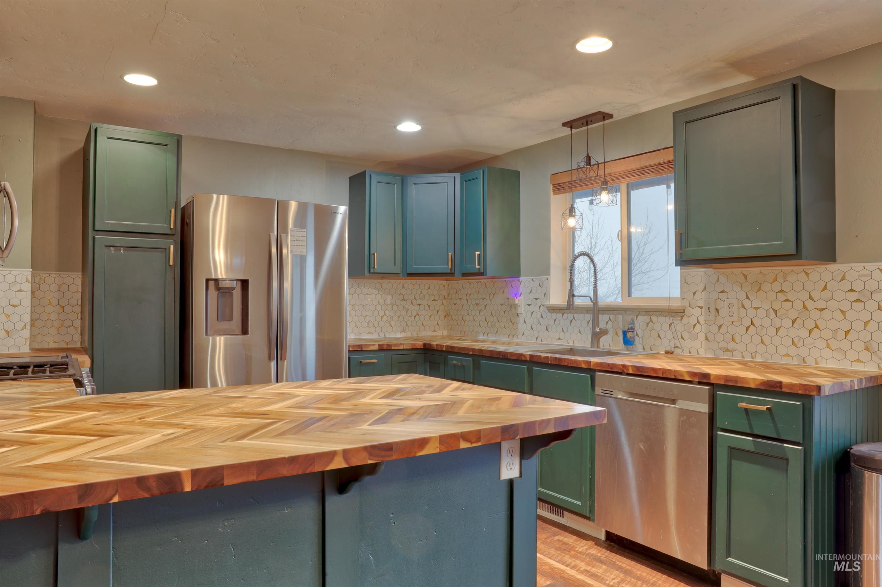Kitchen with green cabinetry, butcher block countertops, stainless steel appliances, pendant lighting, and tasteful backsplash