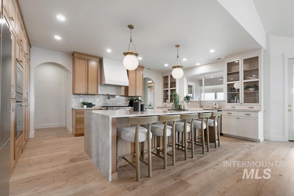 Kitchen featuring arched walkways, a breakfast bar area, light stone counters, pendant lighting, and light wood-type flooring