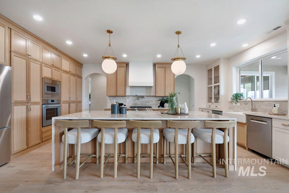 Kitchen with arched walkways, light stone counters, stainless steel appliances, light wood-style flooring, and light brown cabinetry