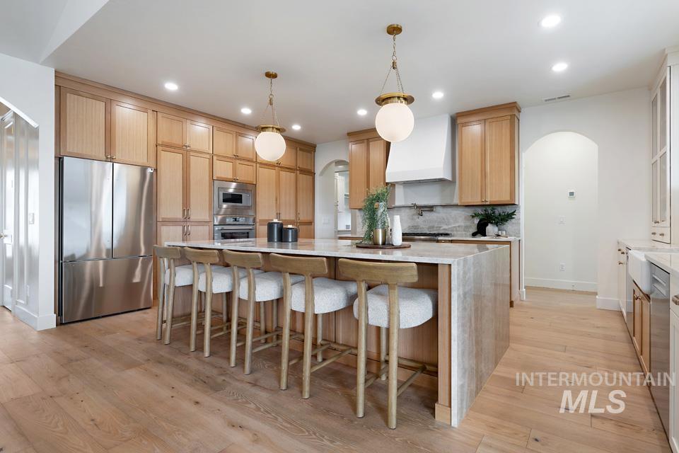 Kitchen featuring arched walkways, appliances with stainless steel finishes, light stone counters, a kitchen bar, and custom range hood