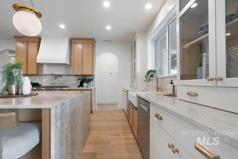 Kitchen featuring arched walkways, light stone countertops, backsplash, light wood-type flooring, and recessed lighting