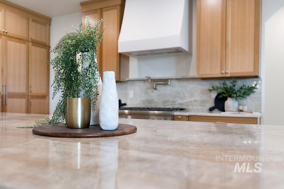 Kitchen view of decorative backsplash, premium range hood, pot filler, light stone counters, and light brown cabinetry