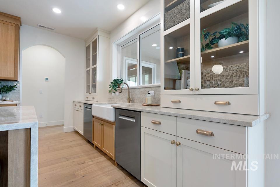 Kitchen featuring light stone countertops, arched walkways, light wood finished floors, stainless steel dishwasher, and recessed lighting