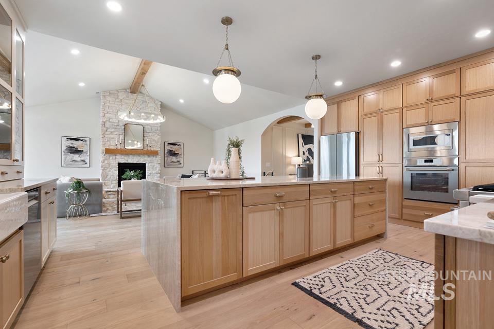 Kitchen with light brown cabinets, arched walkways, appliances with stainless steel finishes, light stone countertops, and recessed lighting