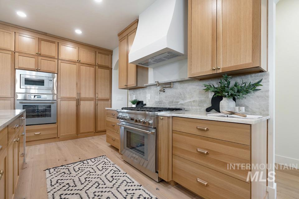 Kitchen featuring wall chimney exhaust hood, stainless steel appliances, light brown cabinetry, backsplash, and recessed lighting