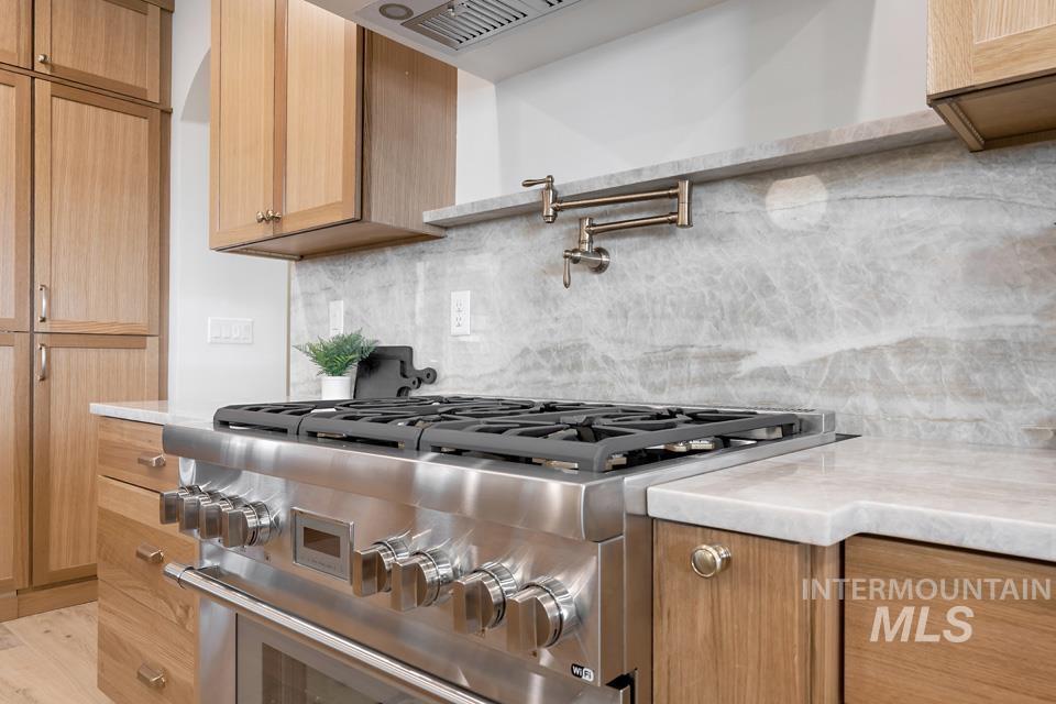 Kitchen with decorative backsplash, high end stainless steel range, and light stone countertops