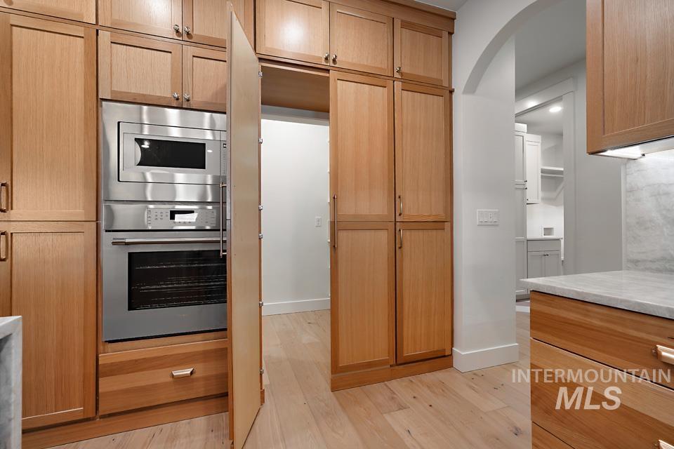 Kitchen featuring stainless steel appliances, light wood-style floors, arched walkways, light stone countertops, and light brown cabinets