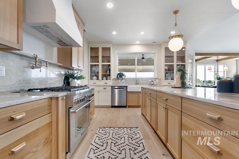 Kitchen with light brown cabinets, appliances with stainless steel finishes, wall chimney exhaust hood, light stone countertops, and beam ceiling