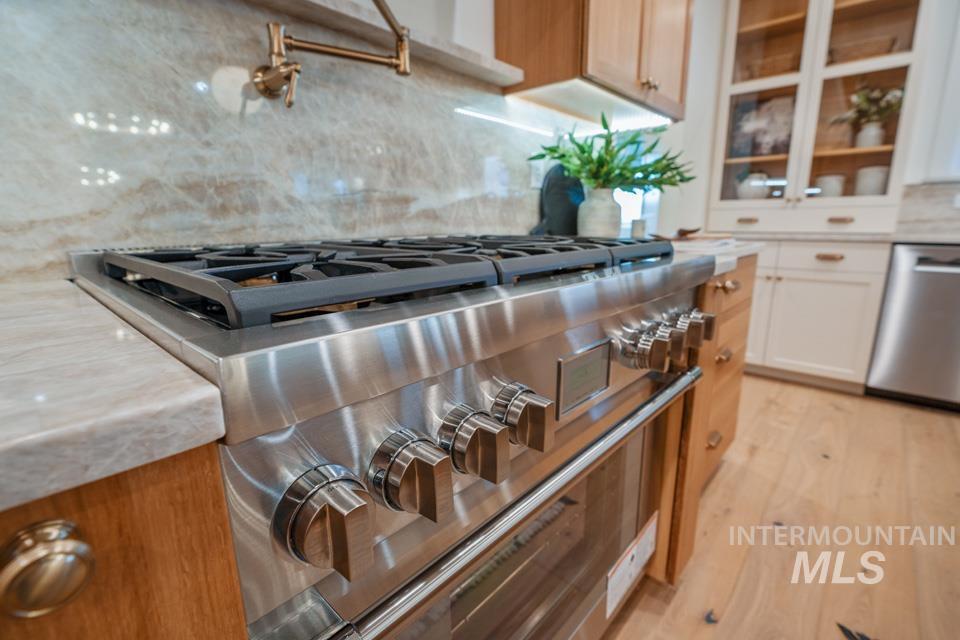 Kitchen with decorative backsplash, stainless steel appliances, light wood-type flooring, brown cabinets, and light stone countertops