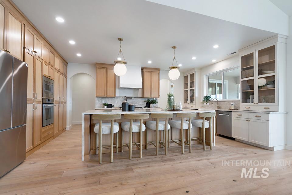Kitchen featuring hanging light fixtures, a kitchen breakfast bar, a center island, stainless steel appliances, and light wood-style floors