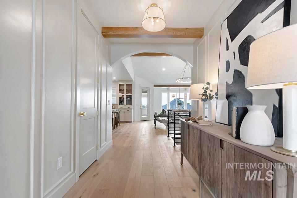Corridor featuring arched walkways, light wood-style flooring, and beamed ceiling
