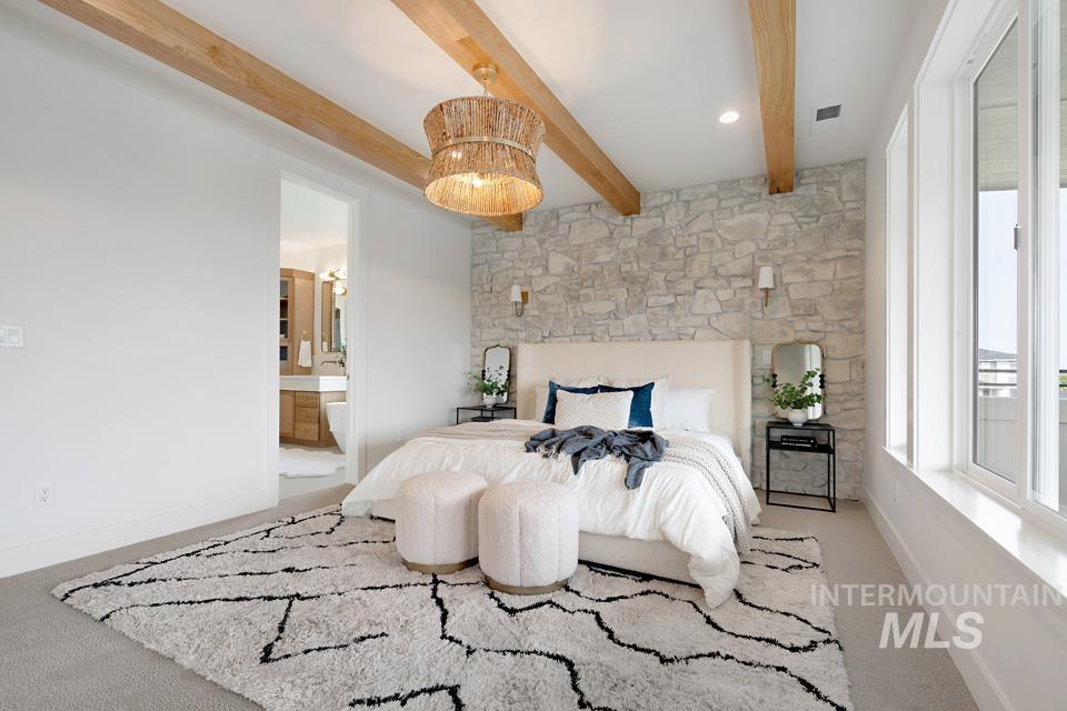 Bedroom featuring light colored carpet, beamed ceiling, and ensuite bath