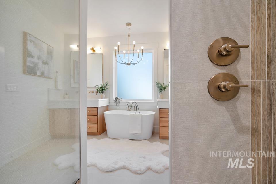Full bathroom featuring vanity, a soaking tub, a shower stall, and a chandelier